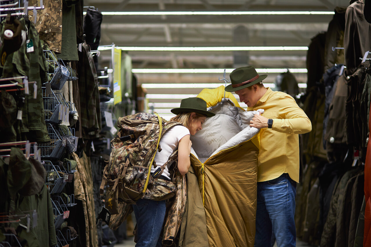 Retkeilijät vertailevat makuupussia ulkoiluvarusteliikkeessä, varustevalinta retkeilyyn.