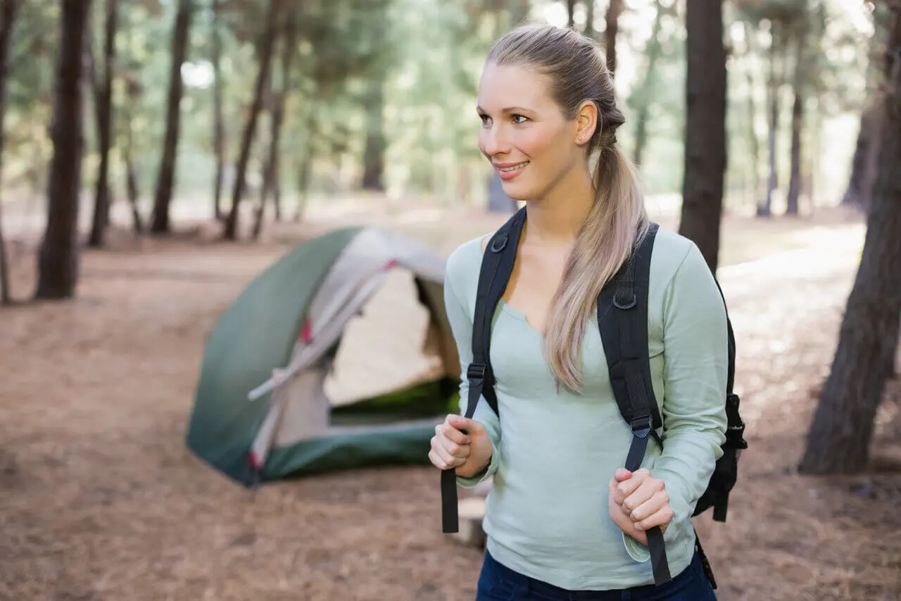 Vaeltaja rinkka selässä metsässä yhden hengen teltan läheisyydessä vaellusretkellä.