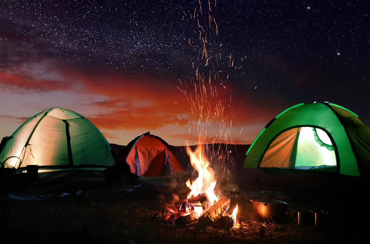 Eri telttatyyppejä pystytettynä leirinuotion ympärille tähtitaivaan alla retkeilyolosuhteissa.