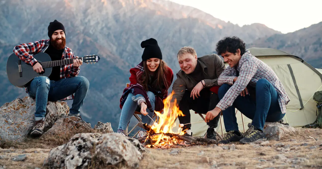 Retkeilijät istuvat nuotion äärellä teltan vieressä retkellä luonnossa.
