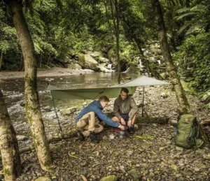 Fjällräven Abisko Tarp Large viritettynä metsään retkeilijöiden suojaksi.