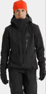 Nainen mustassa Arc'teryx Women’s Alpha SV Jacket -kuoritakissa ja oranssissa pipossa.