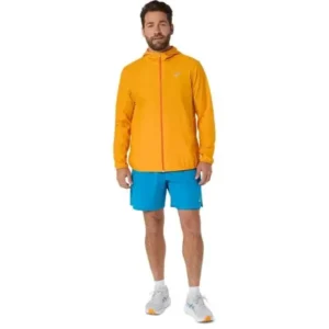 Mies oranssissa juoksutakissa ja sinisissä juoksushortseissa vaalealla taustalla.