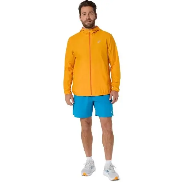 Mies oranssissa juoksutakissa ja sinisissä juoksushortseissa vaalealla taustalla.