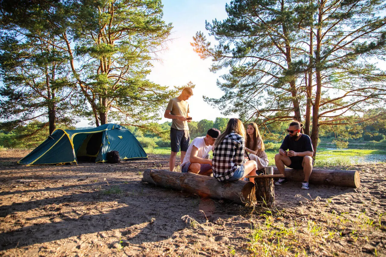 Retkeilijät istuvat nuotion äärellä teltan vieressä metsässä.