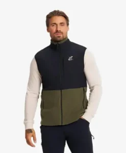 Mies vihreä-mustassa fleece-liivissä vaalealla taustalla.